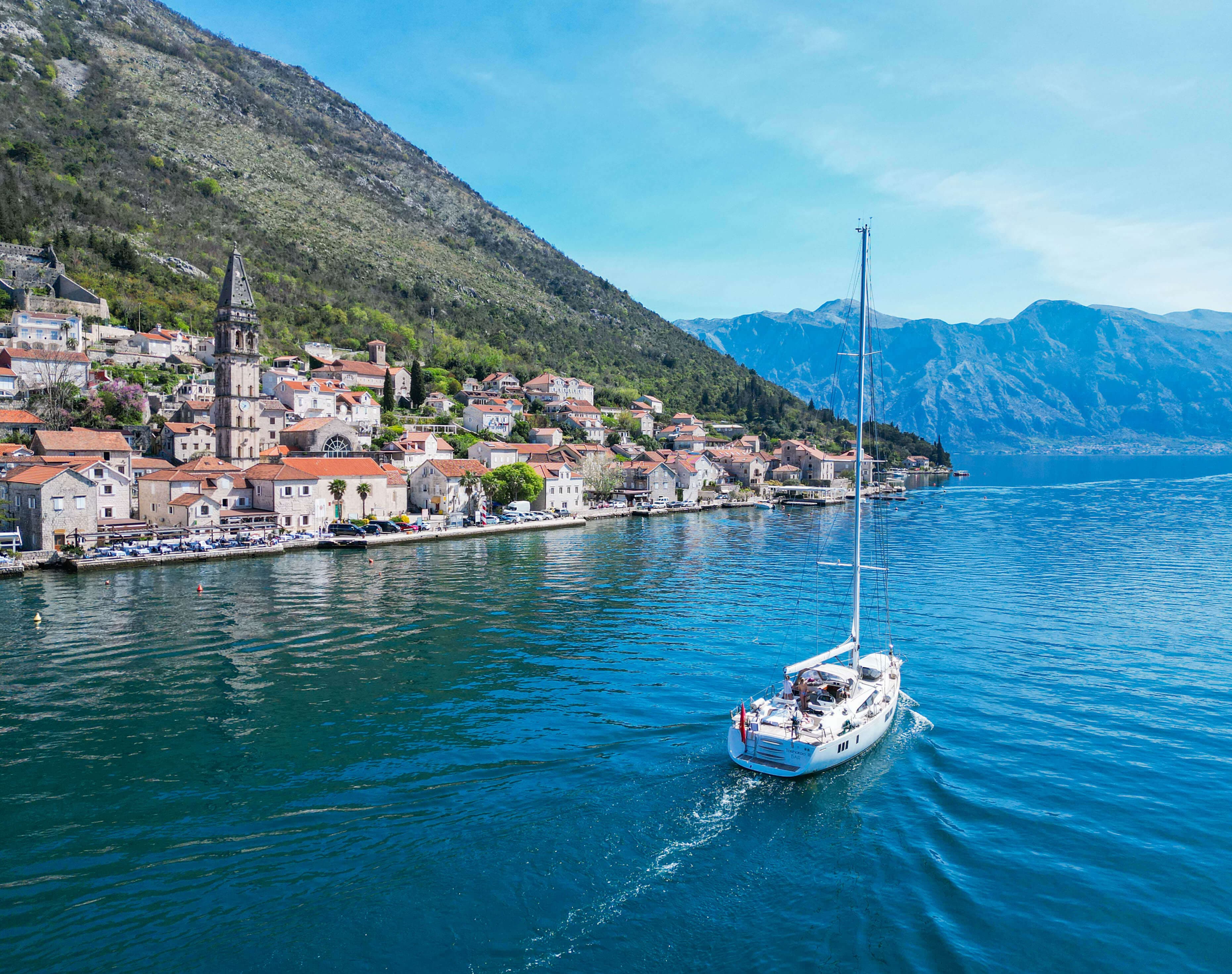 Scenic view of a sailboat on a sea near the coastal town of Perast with red-roofed buildings and mountains