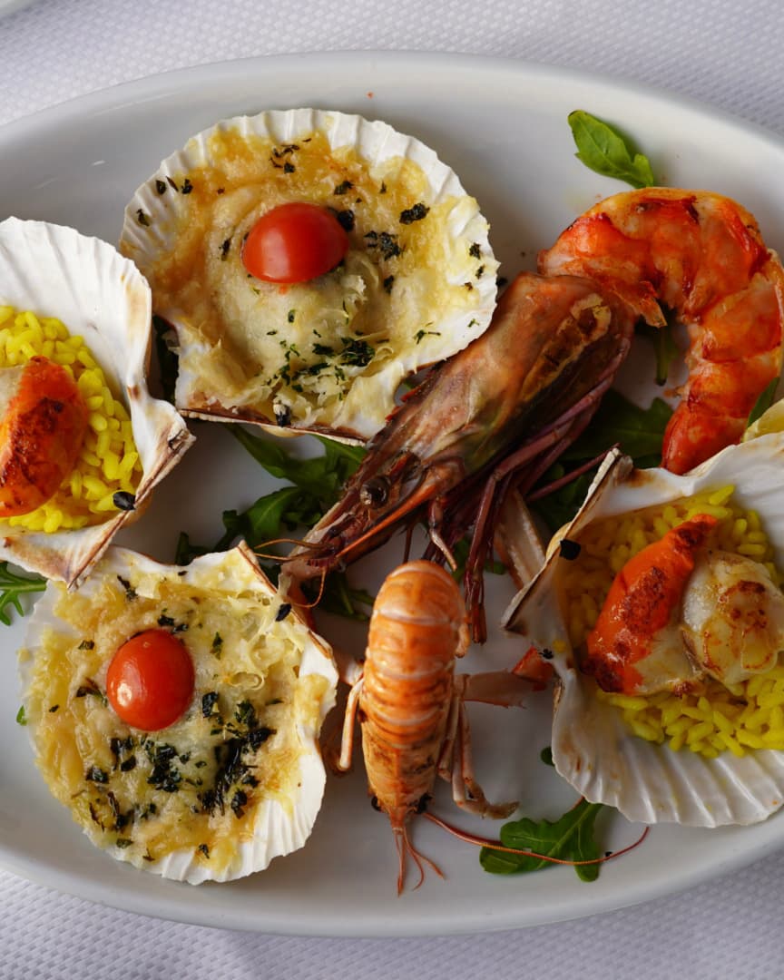 Seafood platter at Hotel Conte's restaurant featuring scallops with cheese and cherry tomatoes, grilled prawns, and shrimp.