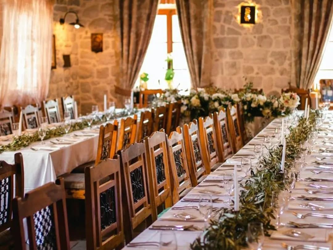 Elegant indoor wedding venue at Hotel Conte, featuring long tables set with white tablecloths, greenery, and candles, against a backdrop of stone walls and large windows.