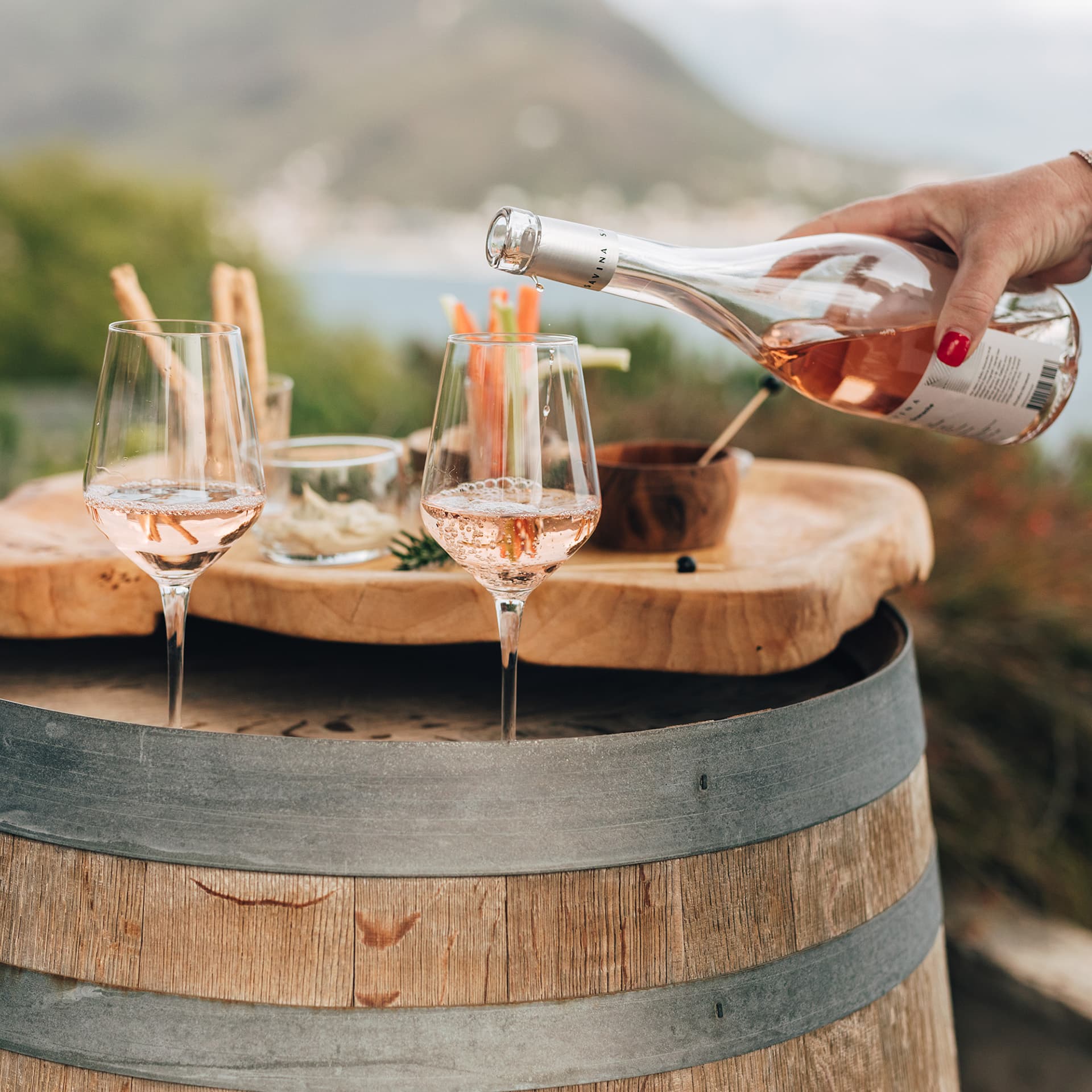 A woman elegantly pours rose wine from a bottle into a crystal glass