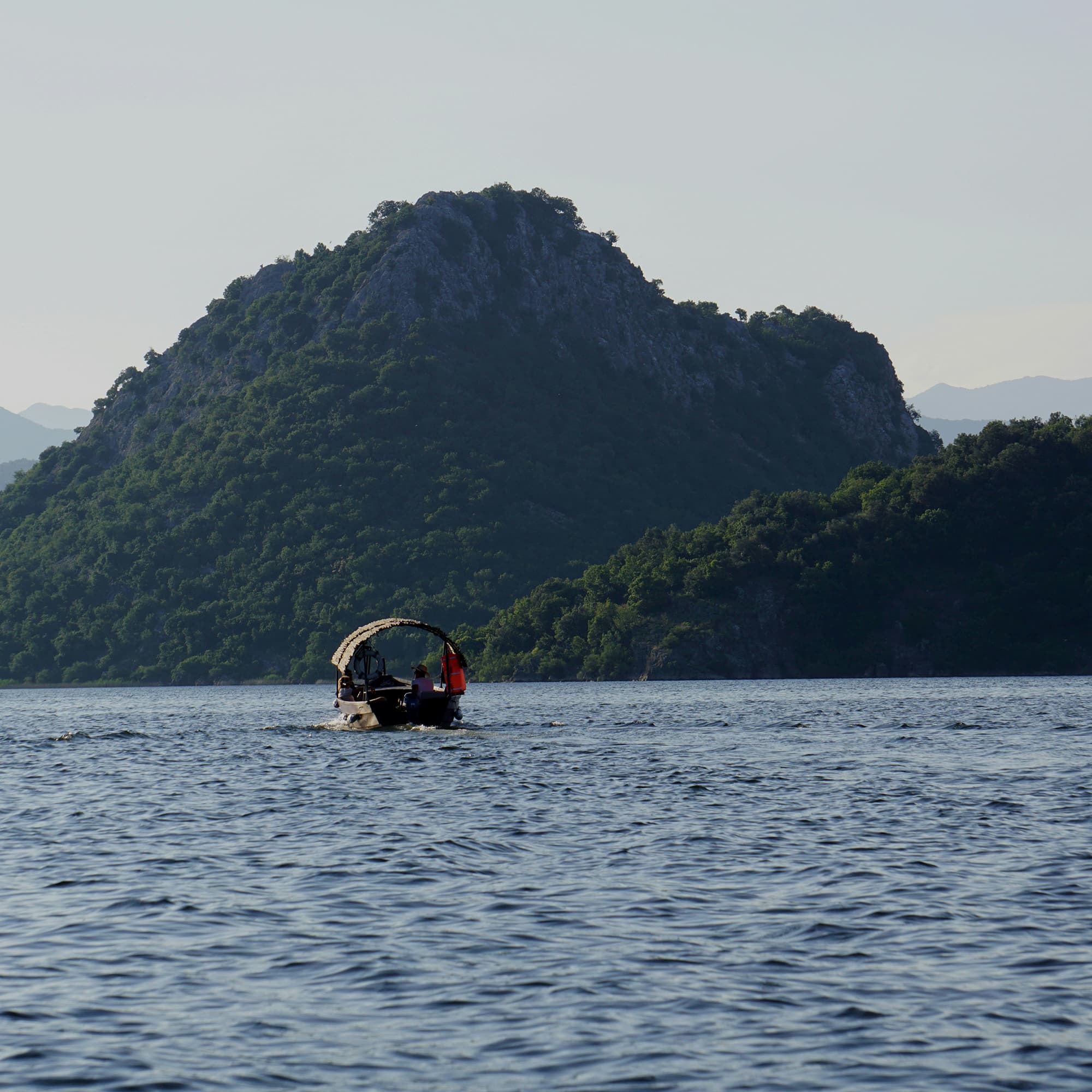 Boat on Skadar Lake with lush, green hills in the background.