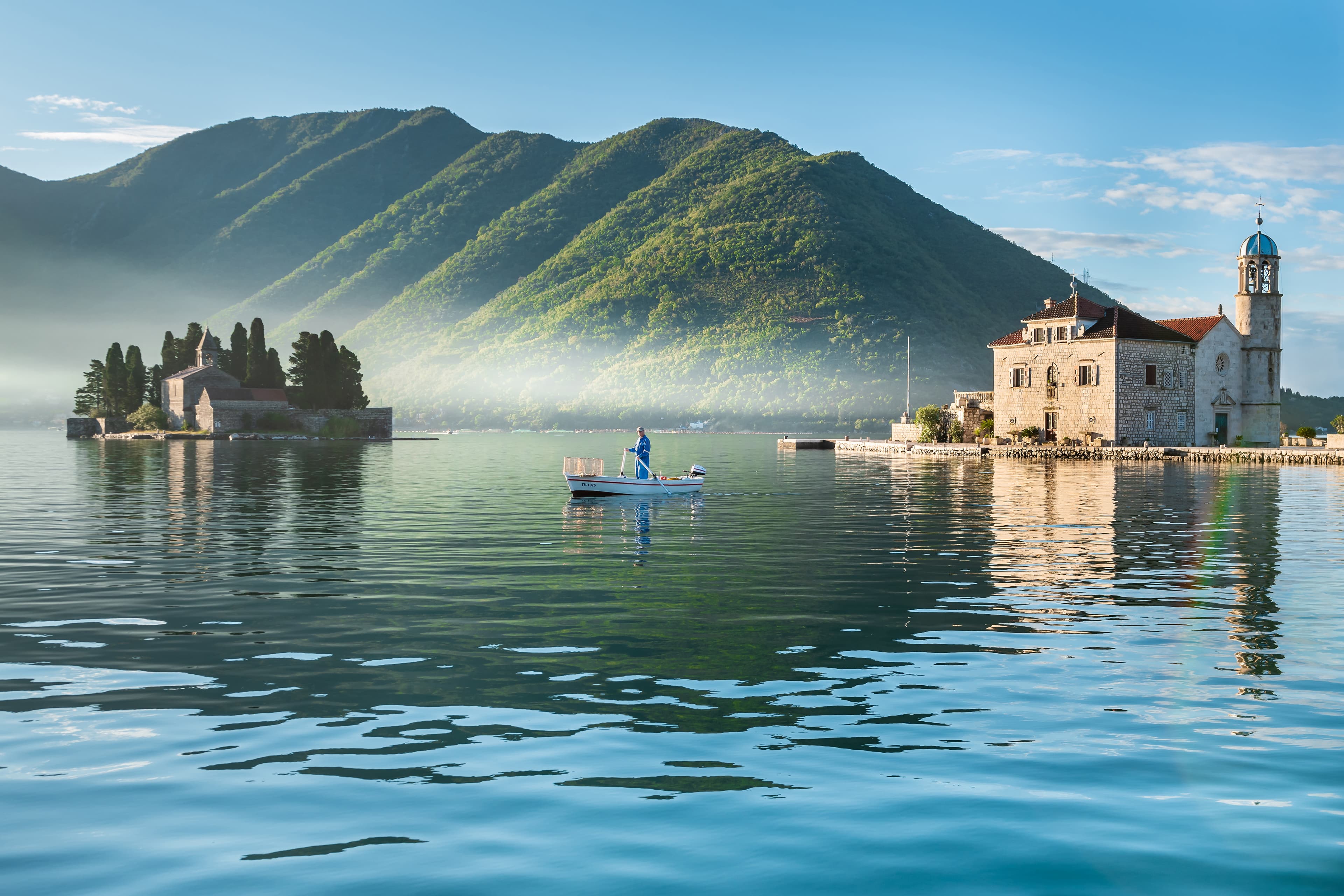 Panoramic view of the Bay of Kotor from Perast, featuring red-roofed buildings, a church tower, and the serene waters with mountainous islands in the background.