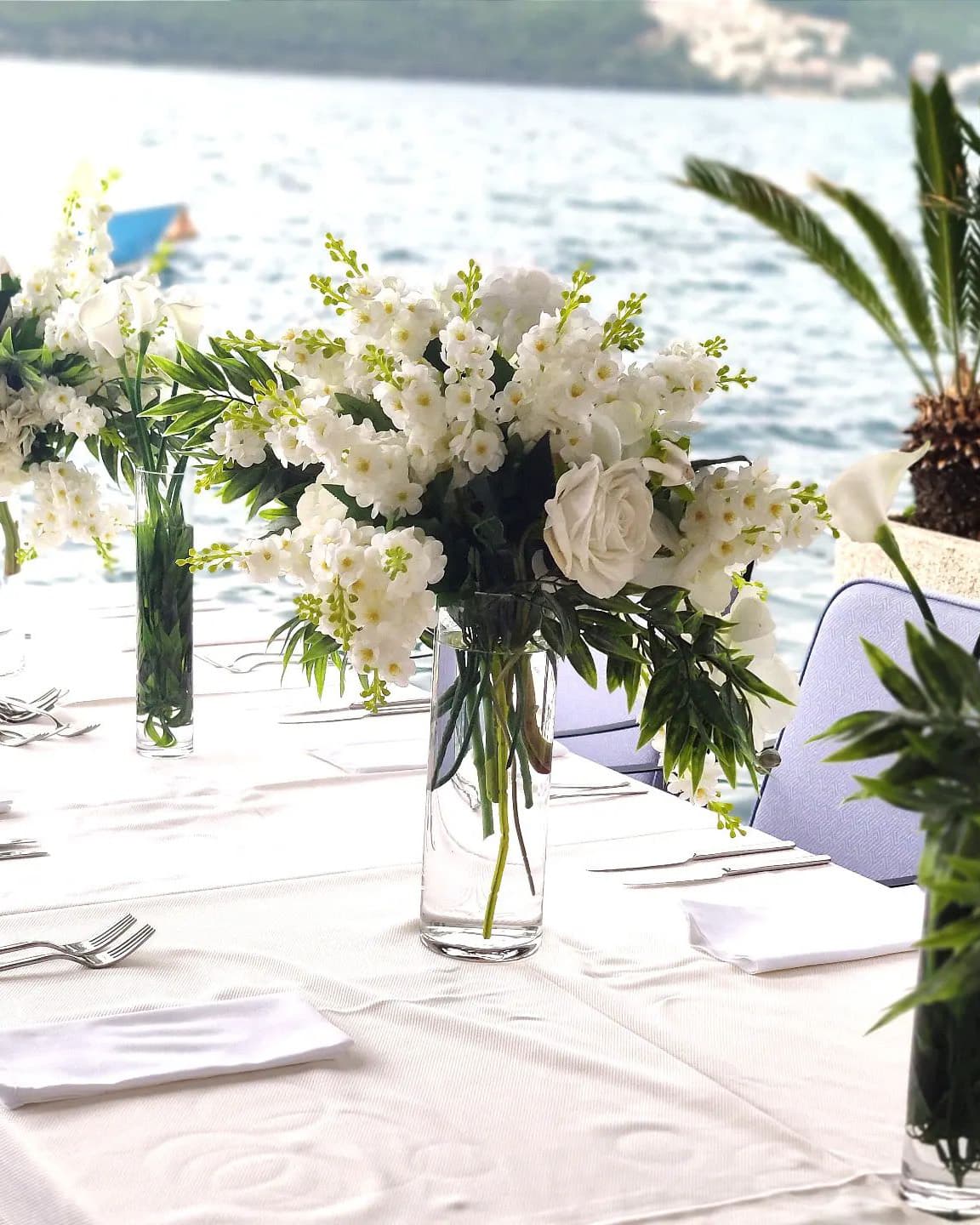 Elegant wedding reception table setup at Hotel Conte, featuring tall floral centerpieces with white flowers and greenery, set against the backdrop of the Bay of Kotor.