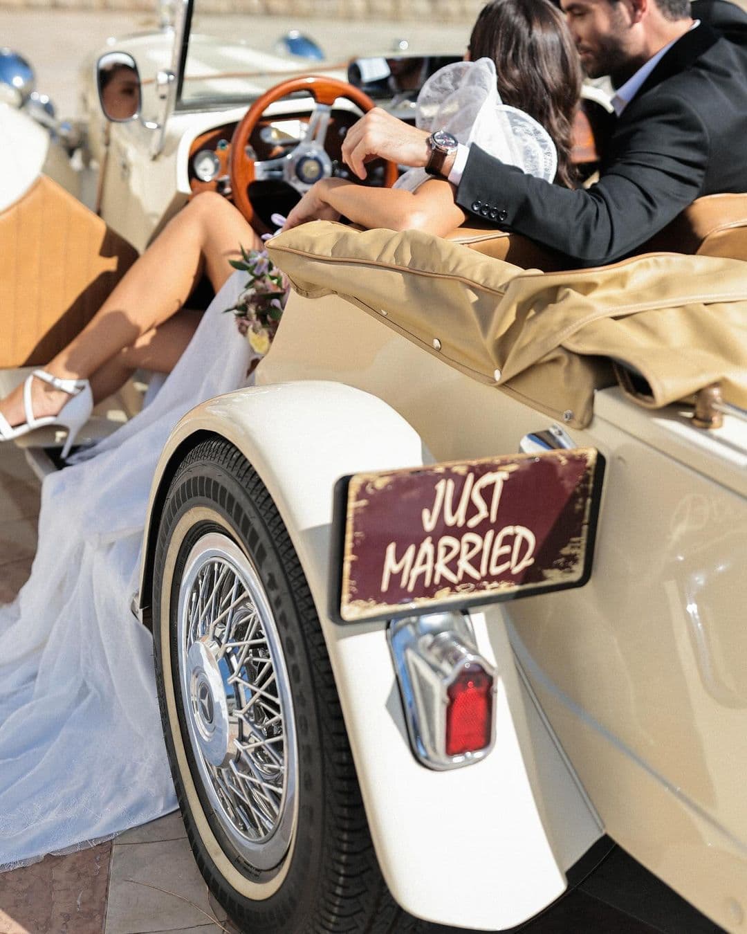 Bride and groom sitting in a vintage car with a 'Just Married' sign