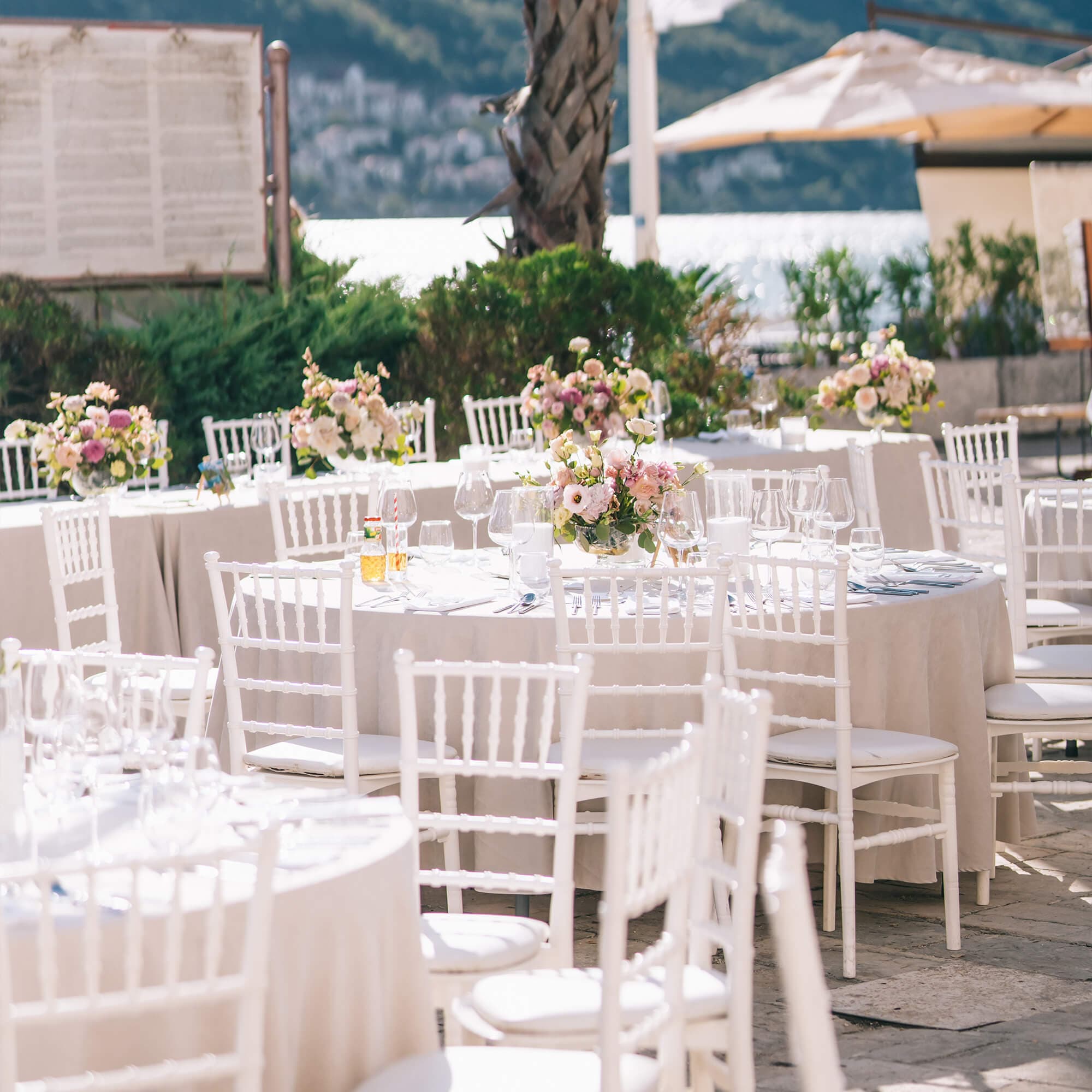 Elegant wedding arch adorned with pink, red, and yellow roses, draped with white fabric, set against a natural outdoor backdrop.