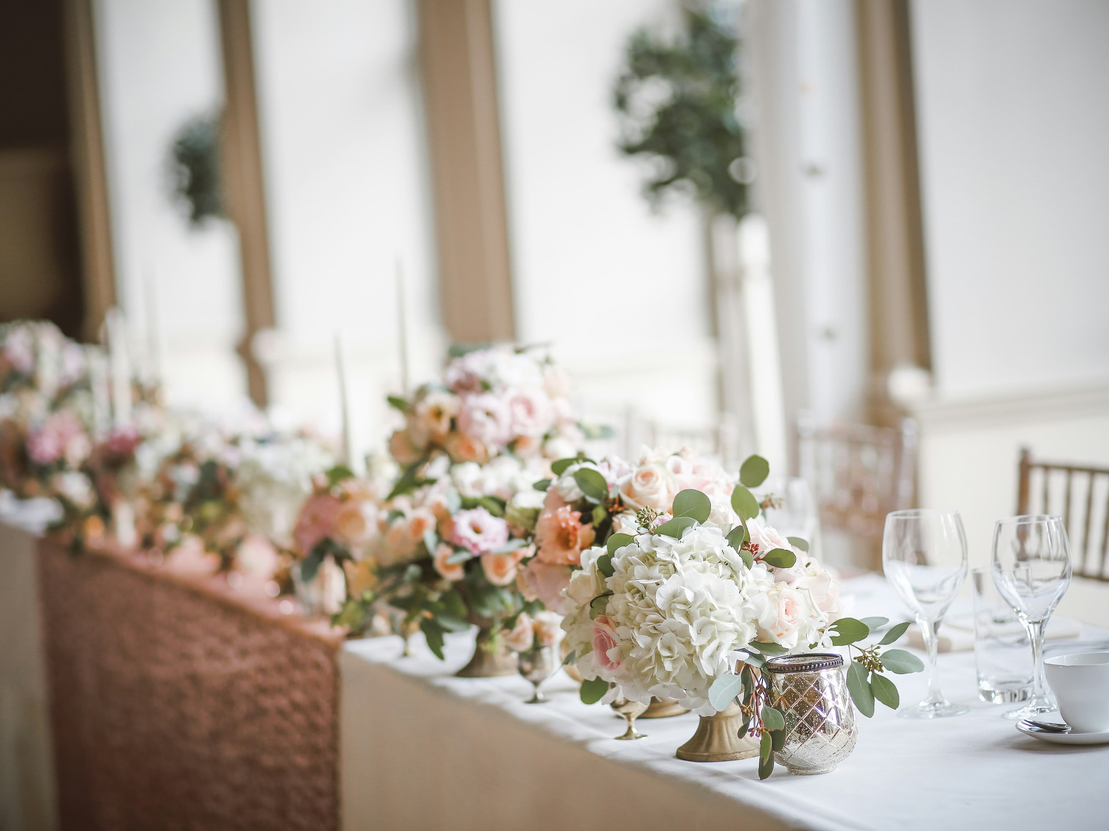 Elegant wedding reception table setup, featuring floral arrangements with pink and white flowers, and neatly arranged glassware.