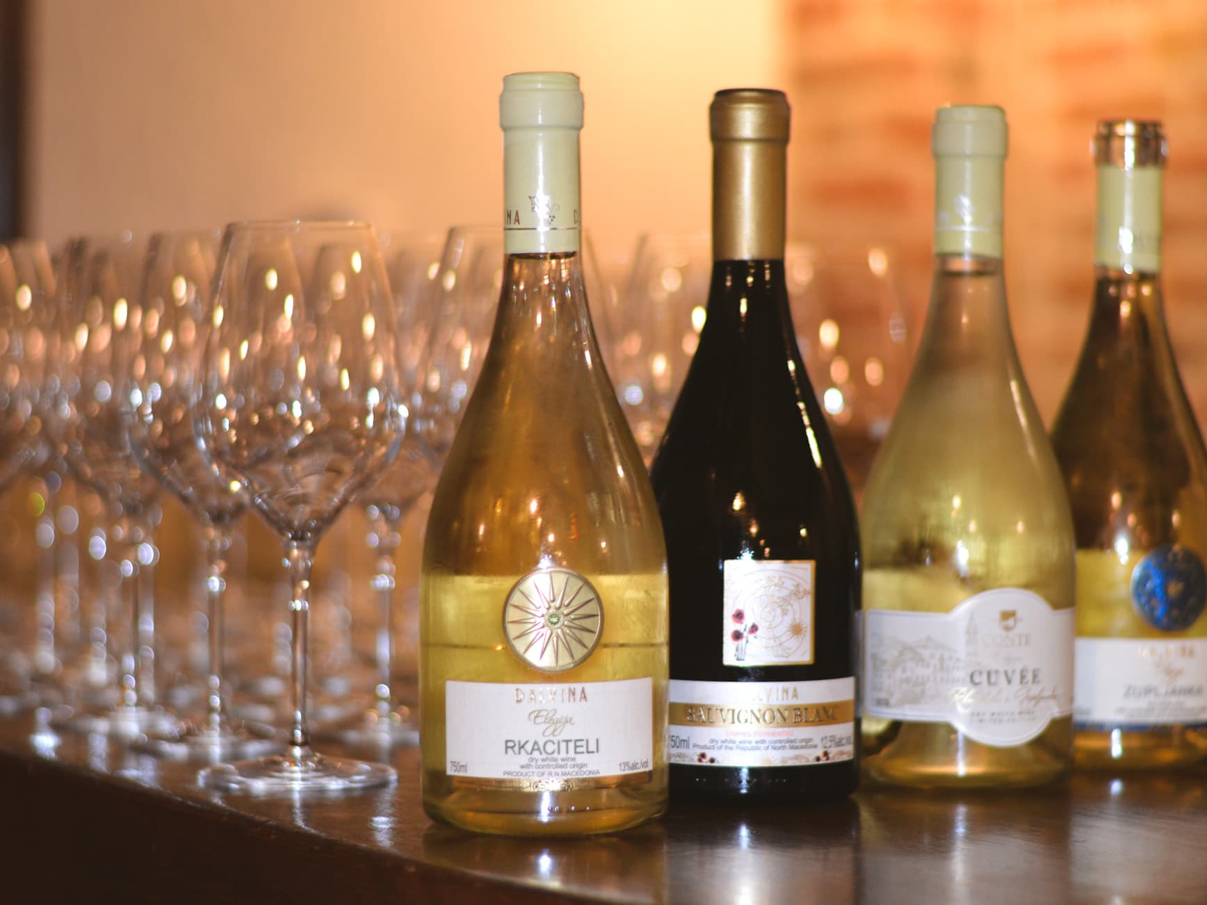 Assorted wine bottles displayed with rows of empty wine glasses at Restaurant Conte.