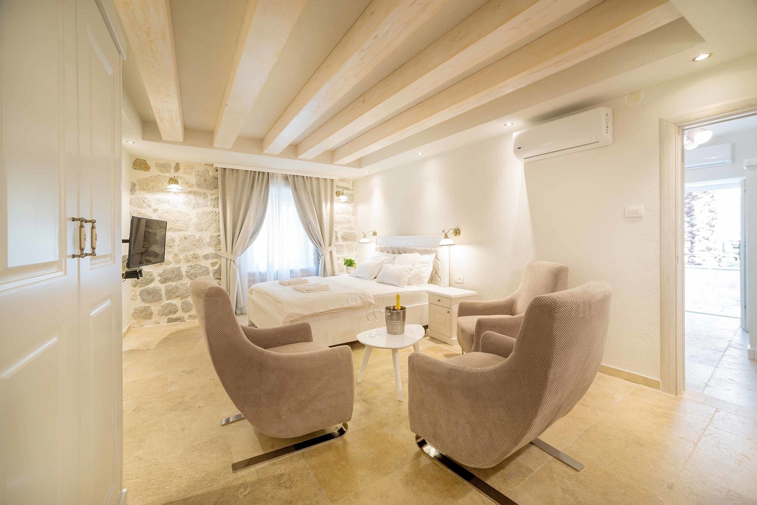 Elegantna hotelska soba u Hotelu Conte sa udobnim krevetom, kamenim zidovima, udobnim prostorom za sjedenje i drvenim gredama na plafonu.